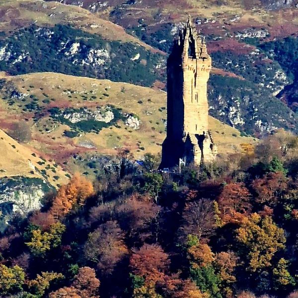 A tall, narrow stone tower stands amidst a landscape of hills and autumnal trees.
