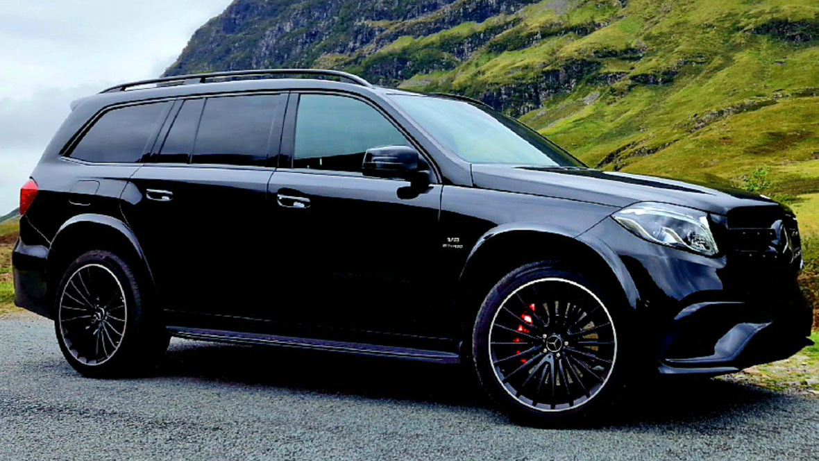 Black SUV parked on a road with green hills in the background. Black SUV parked on a road with green hills in the background.
